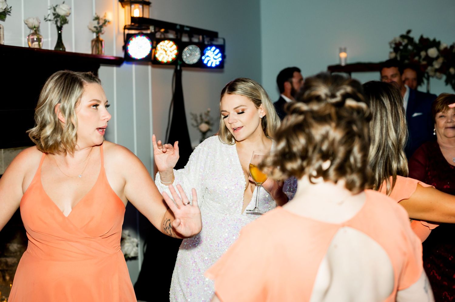 Wedding party members in peach dresses dance and celebrate at an indoor reception.