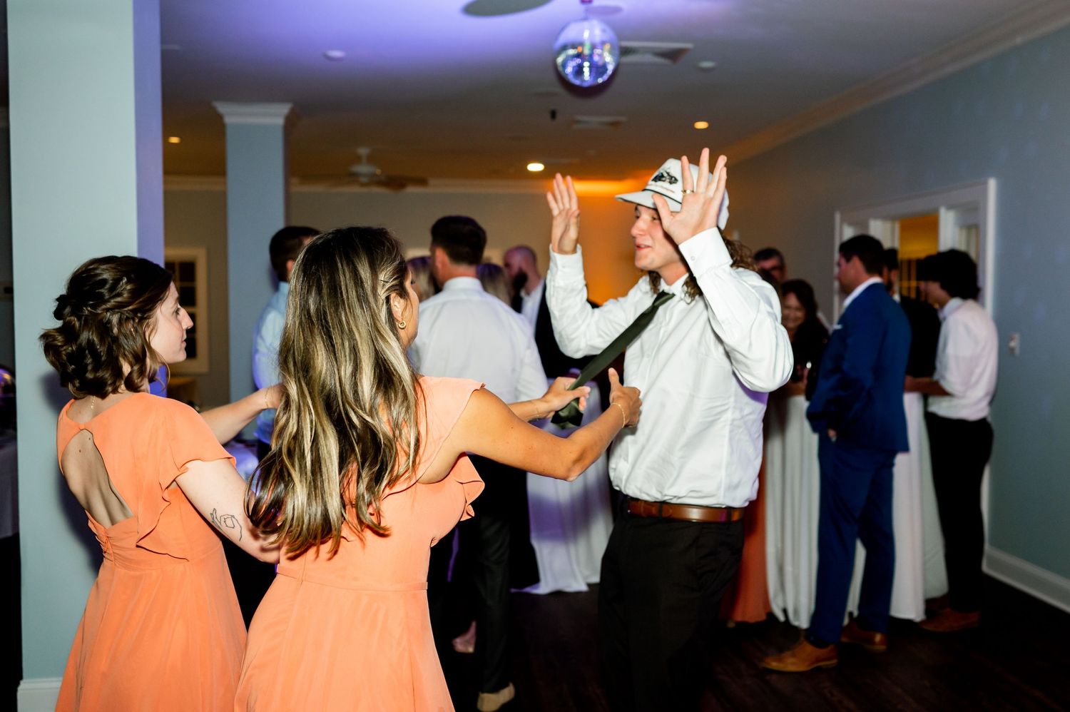 Wedding party members in peach dresses dance with other guests during the reception.