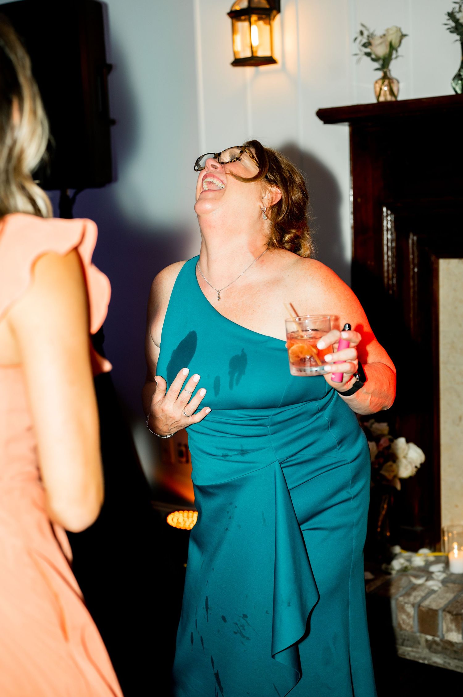 A guest in a teal dress laughs joyfully while holding a cocktail at the reception.