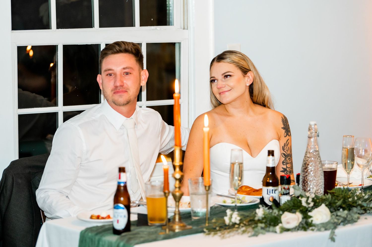 A couple enjoying their wedding cake cutting moment at an intimate indoor reception with candlelit decor.