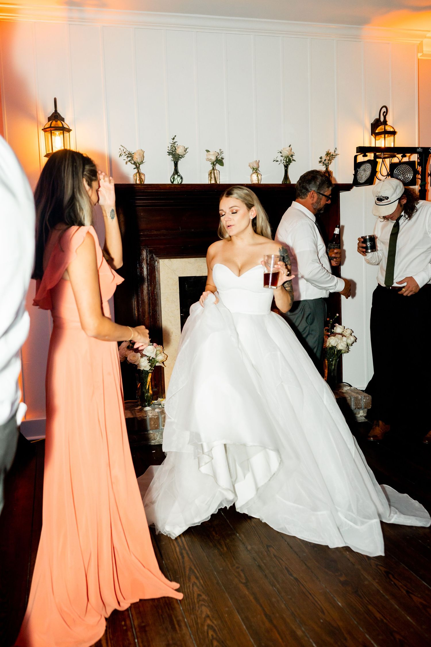 A bride in a white ballgown dances with guests at a wedding reception with decorative lanterns on the wall.