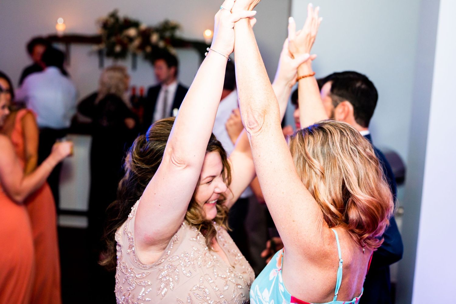 Wedding guests raise their arms while dancing enthusiastically at the reception.