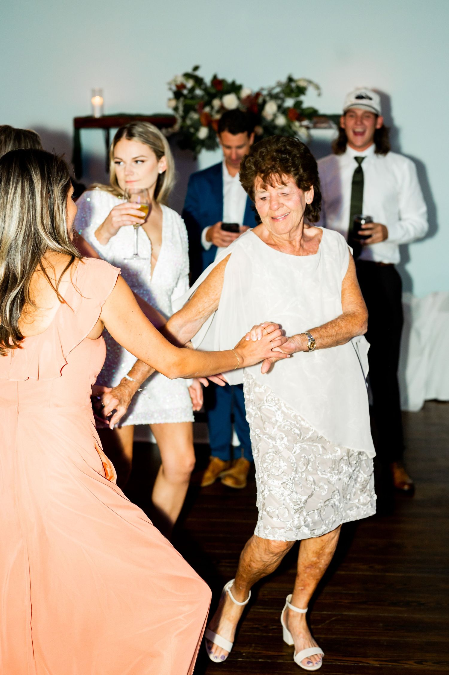 Guests in formal attire dance together on a wooden dance floor at a wedding reception.