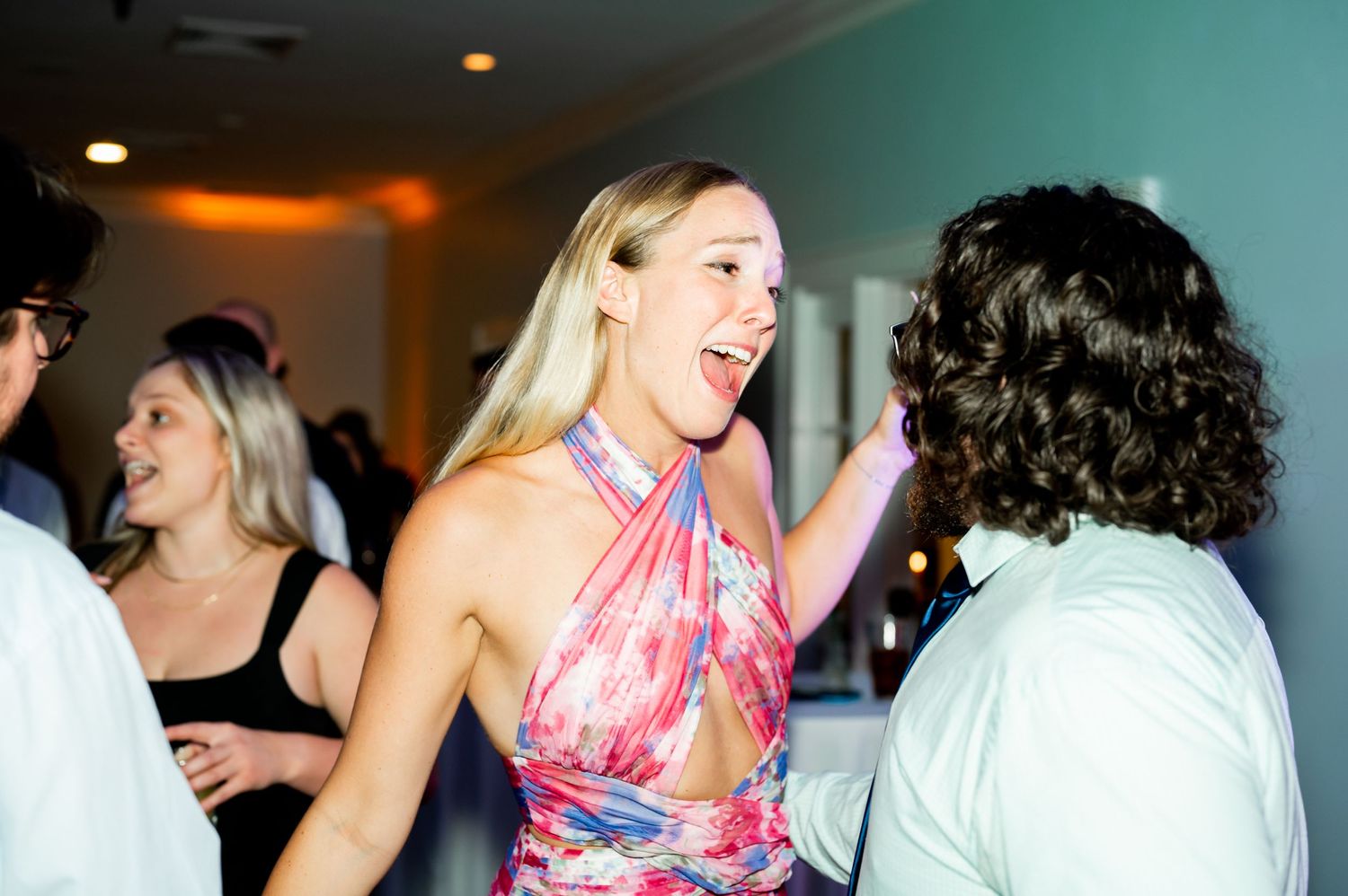 Guests dancing and celebrating at a wedding reception with teal walls.
