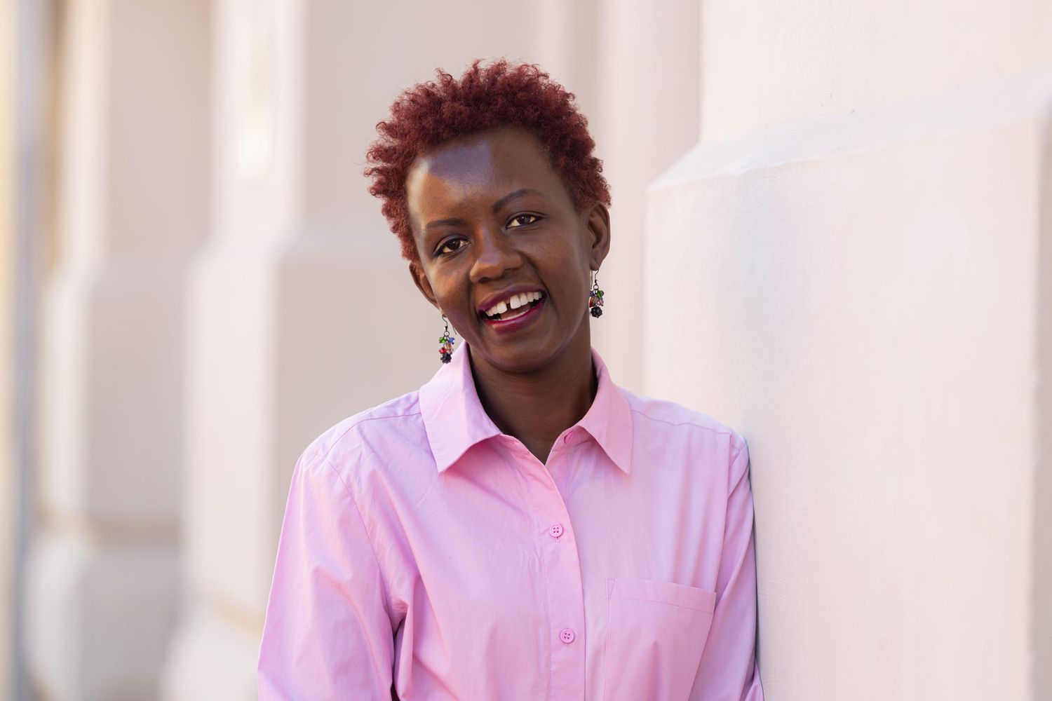 Professional in pink button-down shirt with short red hair smiling warmly at camera.
