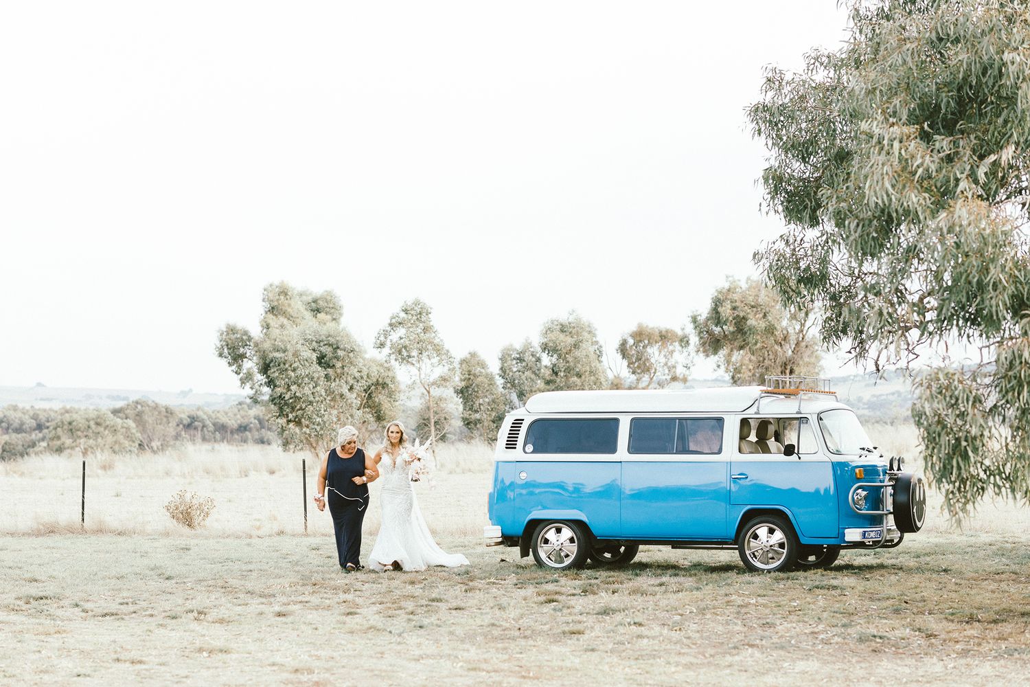 Classic blue and white VW bus parked at outdoor wedding ceremony.