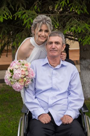 Person in light blue shirt sitting outdoors with pink floral bouquet.