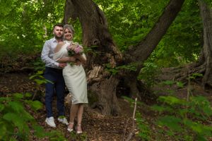 Couple poses together among lush green trees in a forest setting.