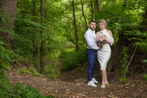 Couple embraces in a serene forest setting with vibrant green foliage.