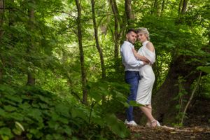 A couple shares an intimate moment in a lush green forest setting during their wedding photoshoot.
