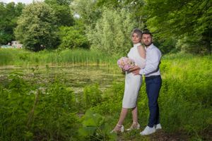 A couple takes romantic photos in a scenic meadow with tall grass and trees.