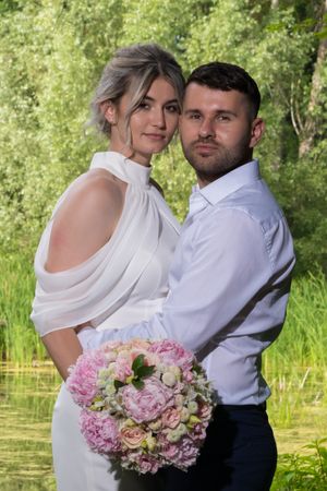 A couple embraces while holding a pink and white wedding bouquet in a garden setting.