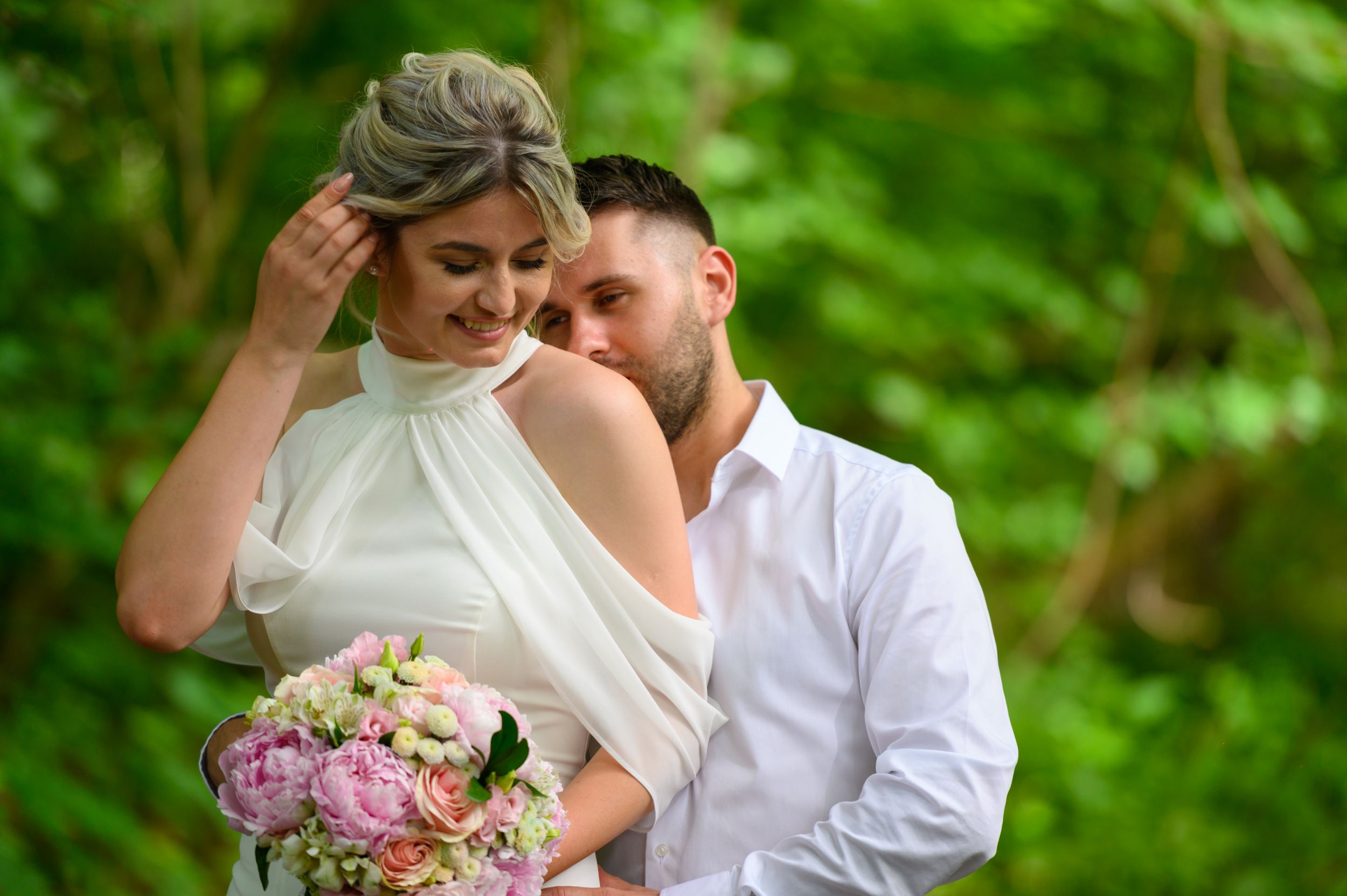 Romantic outdoor photoshoot in a lush green forest setting with delicate pink floral bouquet.