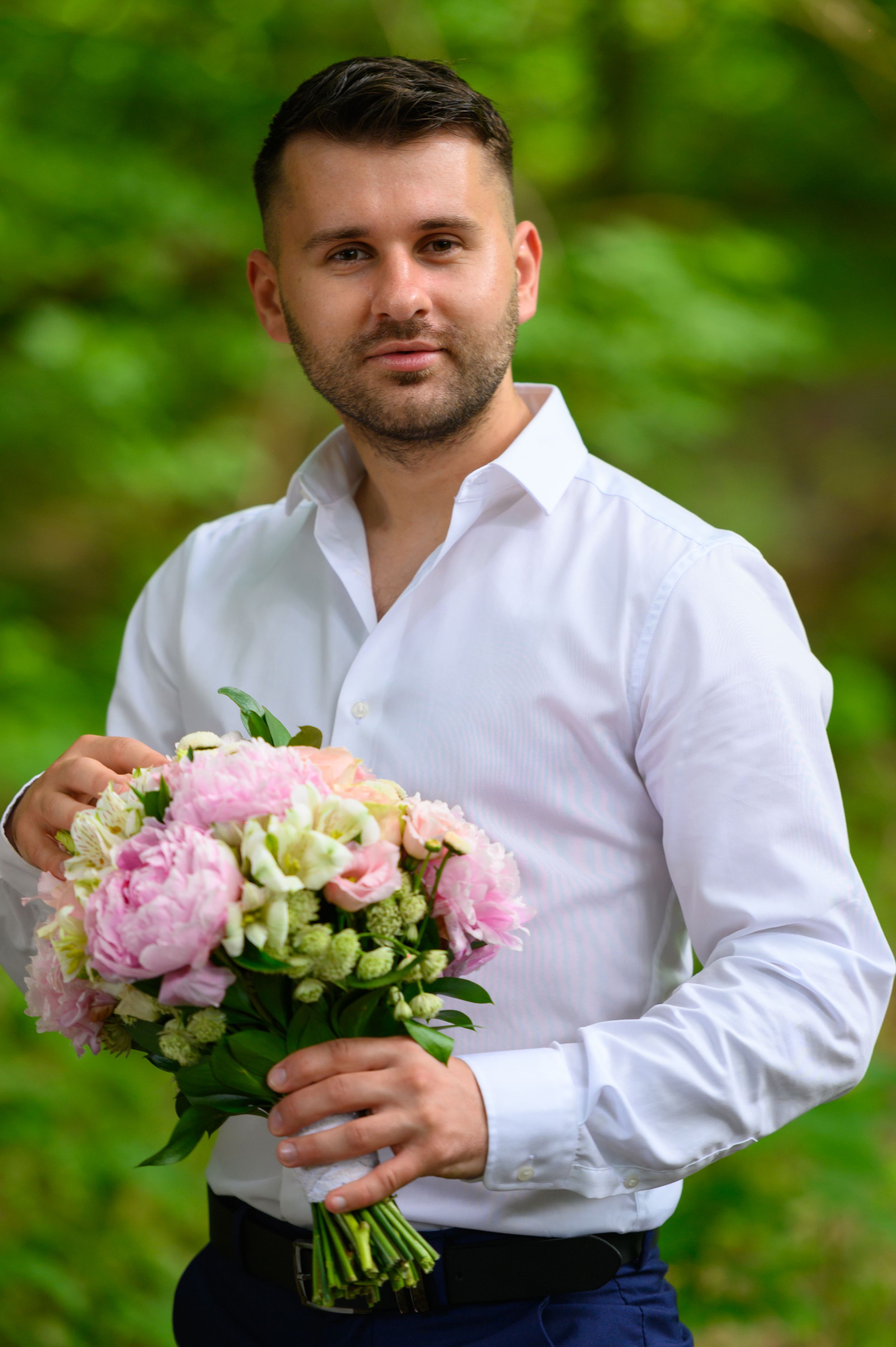 Person in white shirt holding a beautiful pink and white floral bouquet against green background.