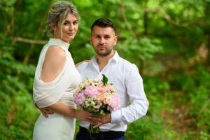 Romantic spring photoshoot with pink flowers against lush green forest backdrop.