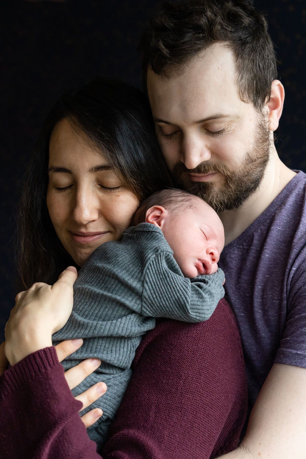 Parents tenderly snuggling with newborn son.