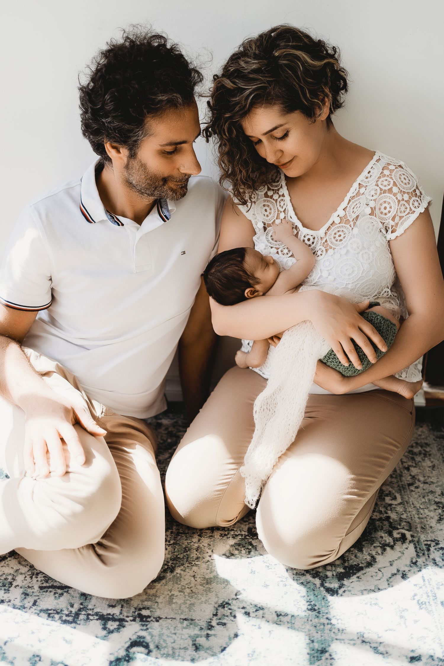 A series of intimate maternity photos showing a couple in white outfits sitting together on a gray rug.