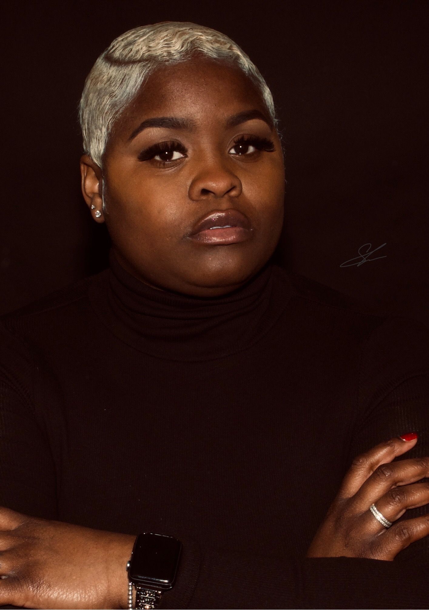 Professional portrait of a person in a black turtleneck against dark background with platinum blonde short hair.