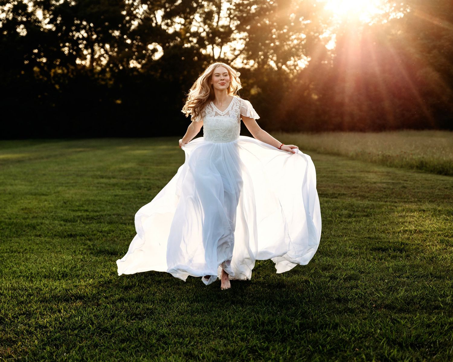 Person in flowing white dress twirling in golden sunset light on grassy field. Middle TN senior photographer