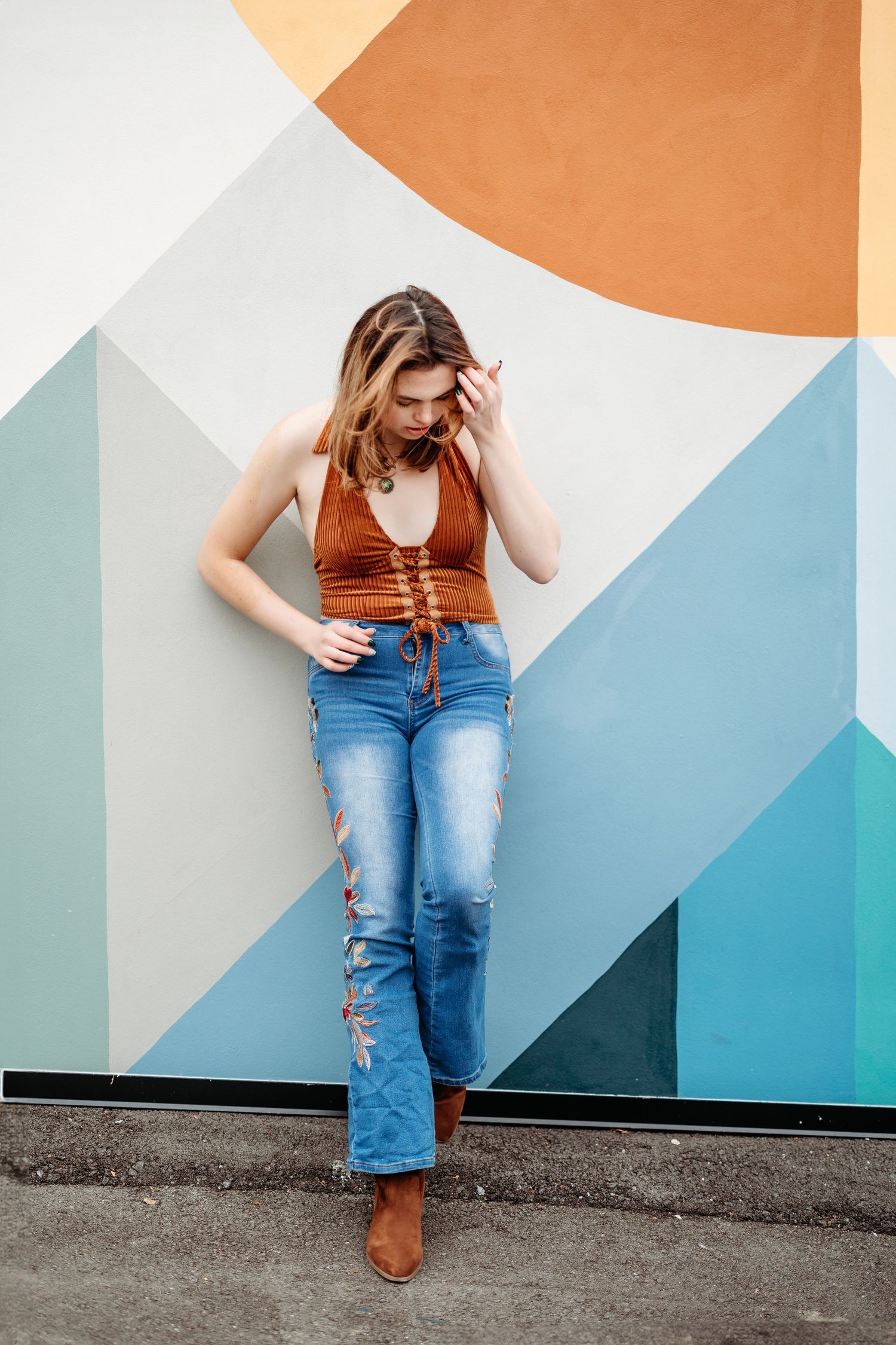 senior wearing brown top and jeans poses against geometric painted wall in casual outdoor photoshoot.Middle TN senior photographer