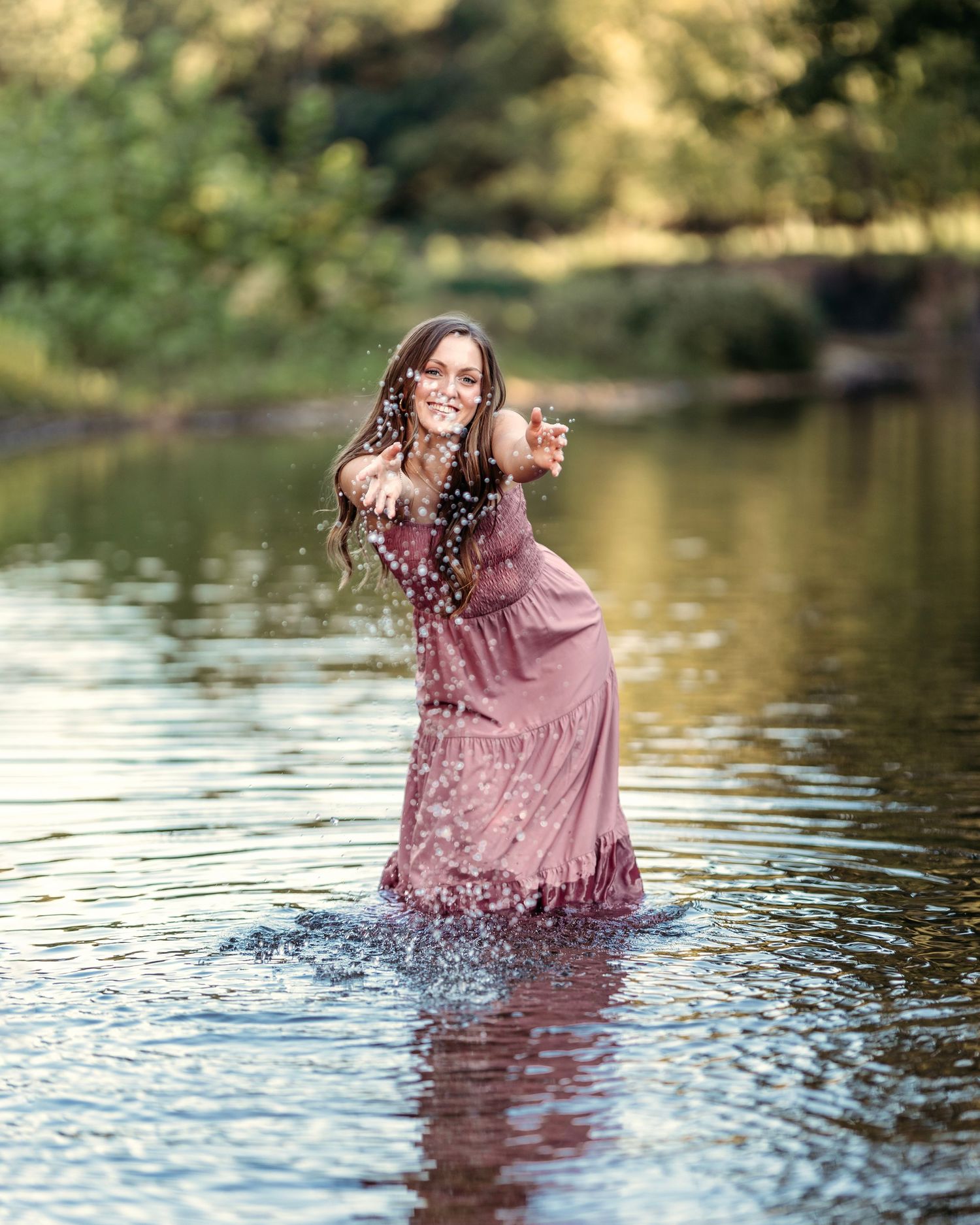 senior girl in a pink dress splashing and playing in a scenic lake at sunset.  Middle TN senior photographer