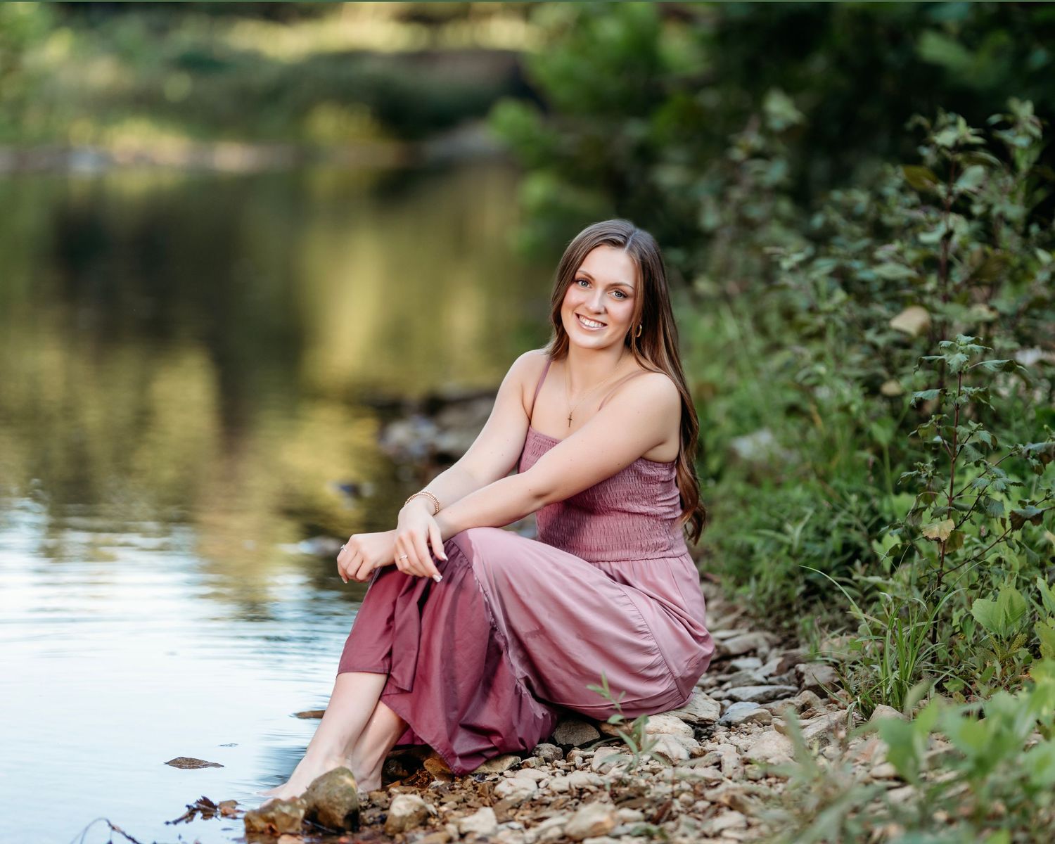 senior girl in a mauve dress posing along a scenic lakeside with natural foliage.  Middle TN senior photographer