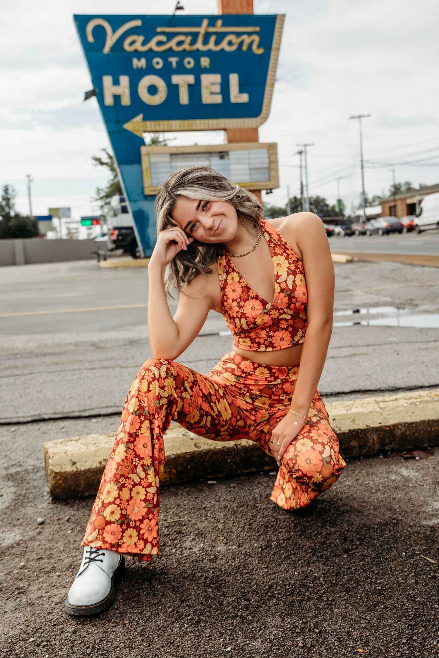 Retro-styled photoshoot near vintage motel sign featuring floral jumpsuit and white sneakers. Middle TN senior photographer