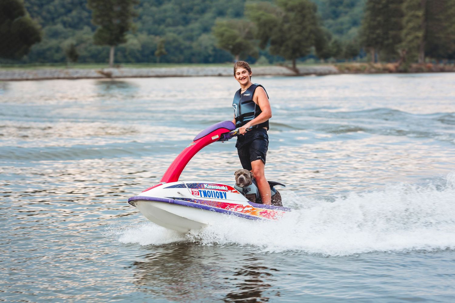 Someone enjoys riding a jet ski across calm waters on a sunny day near forested shores. Middle TN senior photographer