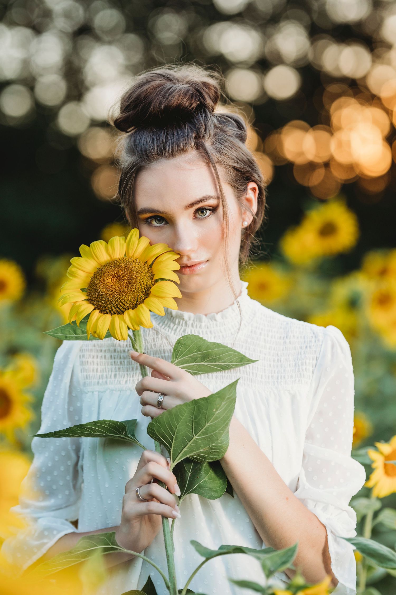 A person in a white lace dress poses playfully with bright yellow sunflowers during a golden hour photoshoot. Middle TN senior photographer