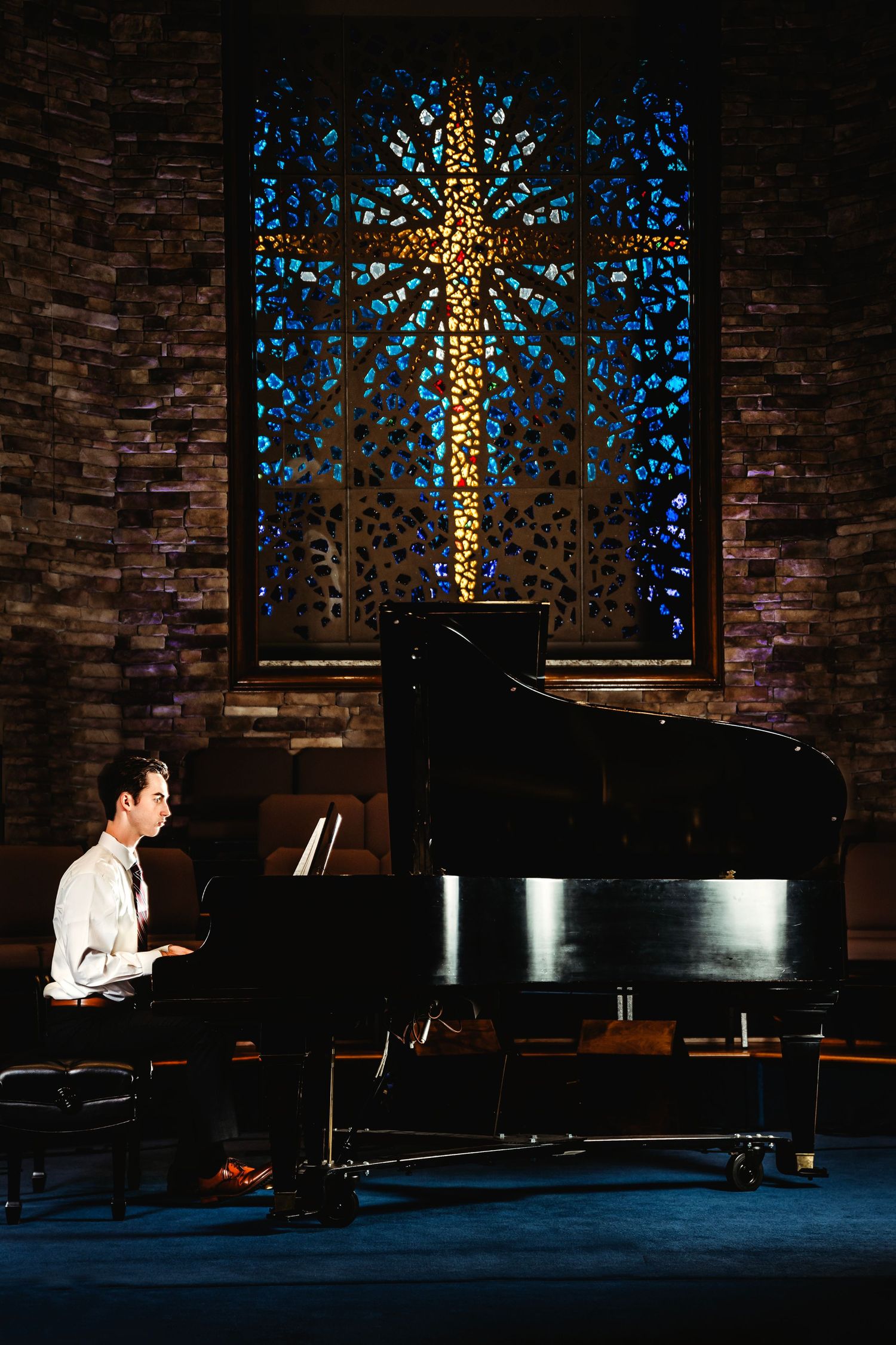 Pianist performing in church with illuminated stained glass cross window.Middle TN senior photographer