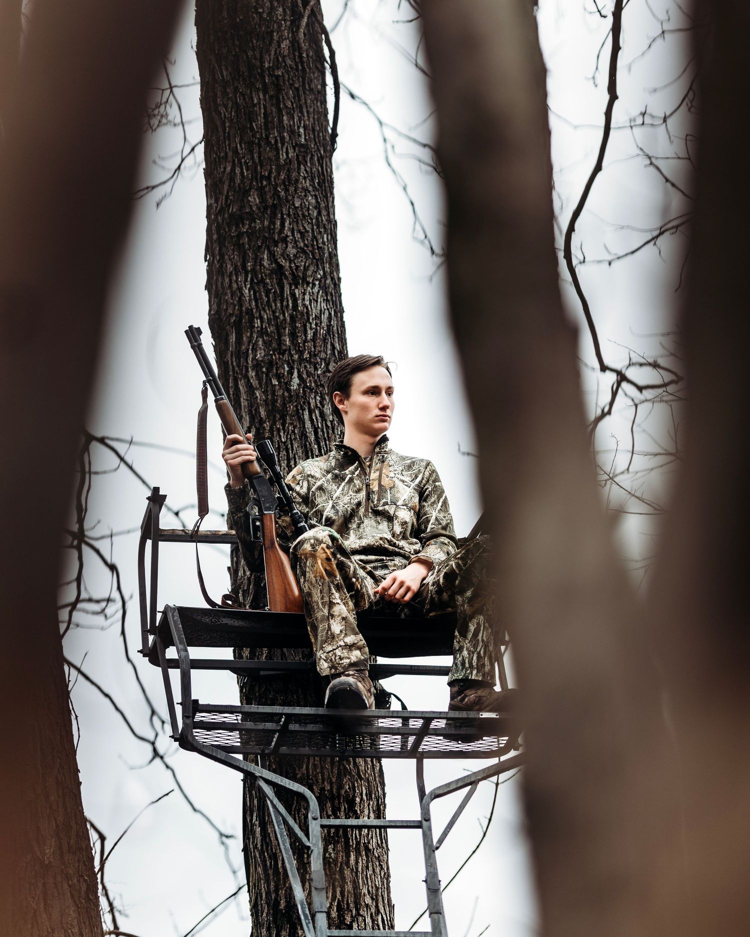 Hunter in camouflage gear positioned in elevated tree stand in forest setting. Middle TN senior photographer