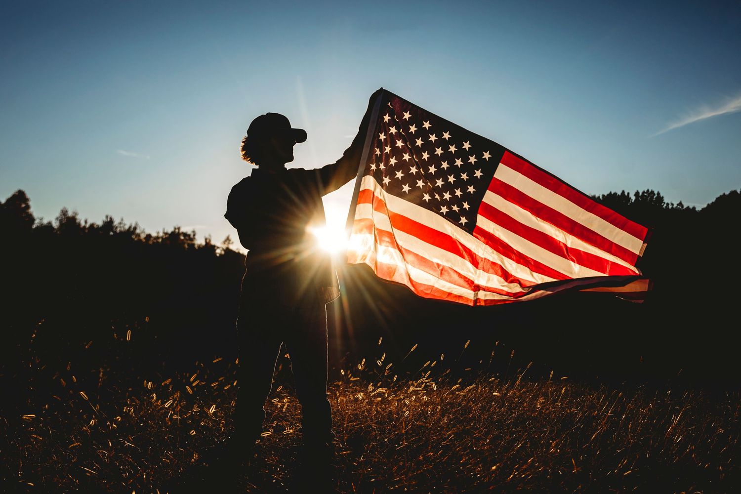 Silhouette of person holding American flag against sunset sky. Middle TN senior photographer