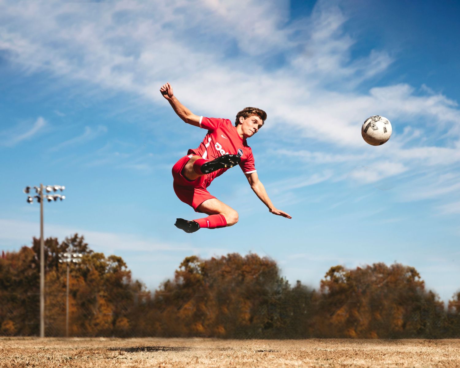 Athletic figure performing dramatic soccer kick against blue sky.Middle TN senior photographer