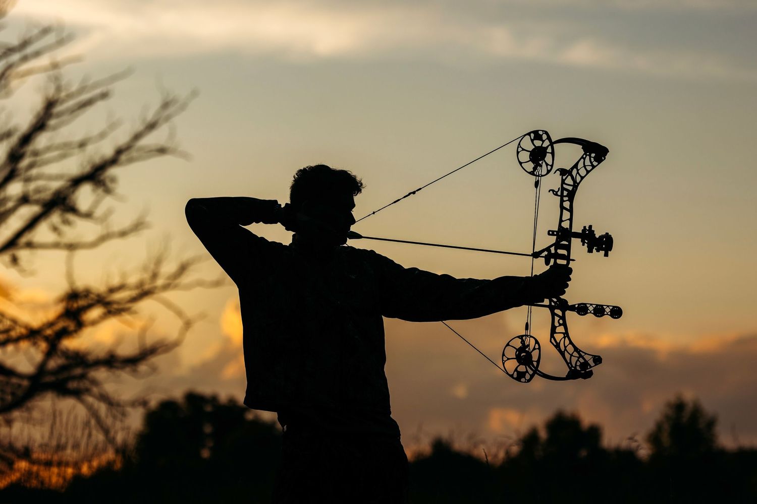 Silhouetted archer practicing with compound bow against dramatic sunset sky. Middle TN senior photographer