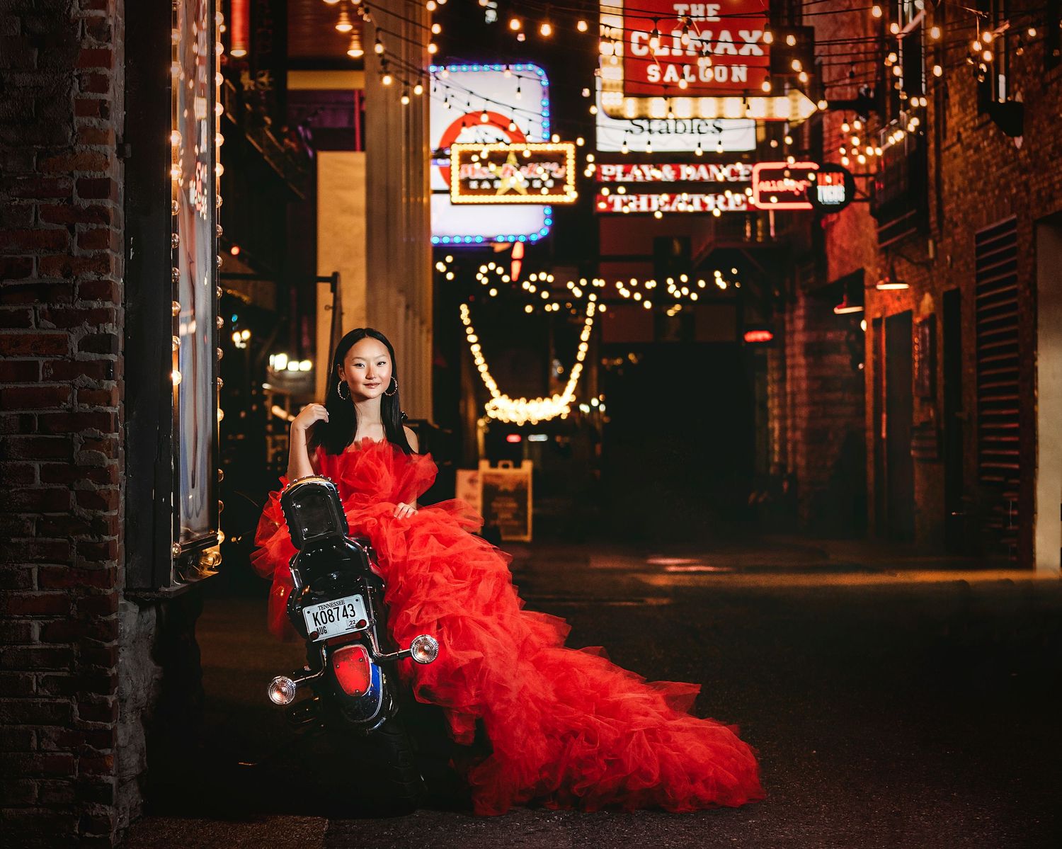 Red flowing dress in an urban nighttime setting with neon lights and brick buildings. Middle TN senior photographer