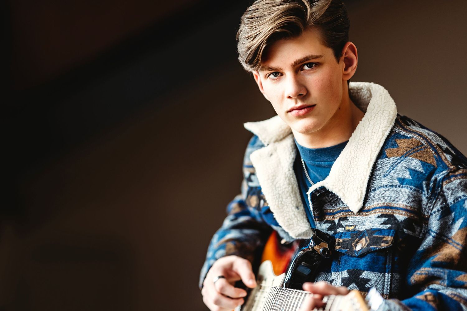 Senior wearing denim jacket in moody indoor portrait setting. Middle TN senior photographer