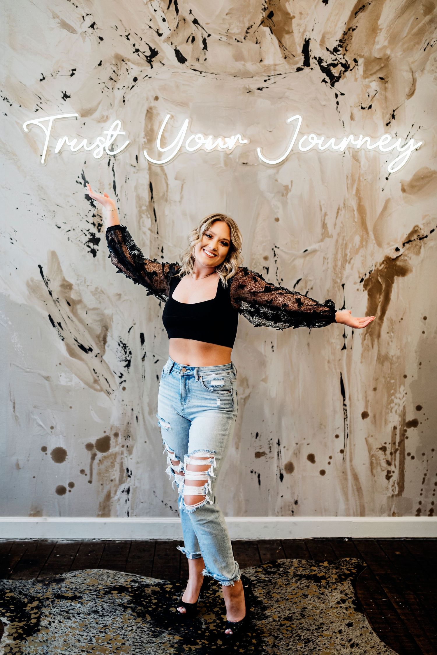 Woman in casual attire posing against textured concrete wall with 'Trust Your Journey' text. Middle TN senior photographer