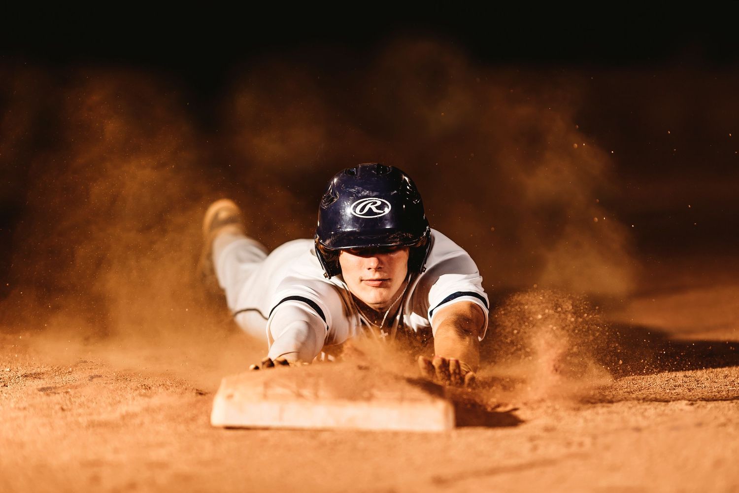 Baseball player slides dramatically into base creating a cloud of dirt and dust. Middle TN senior photographer