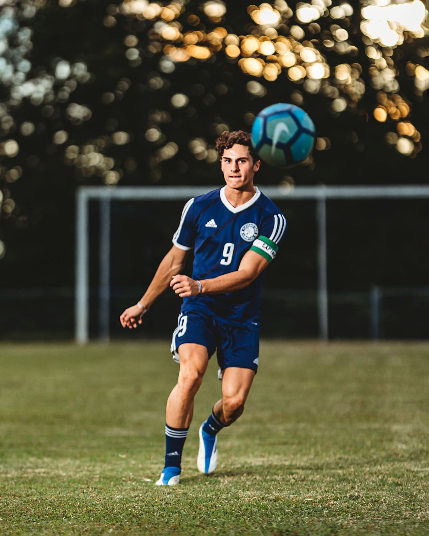 Soccer player in blue jersey running on grass field during golden hour. Middle TN senior photographer