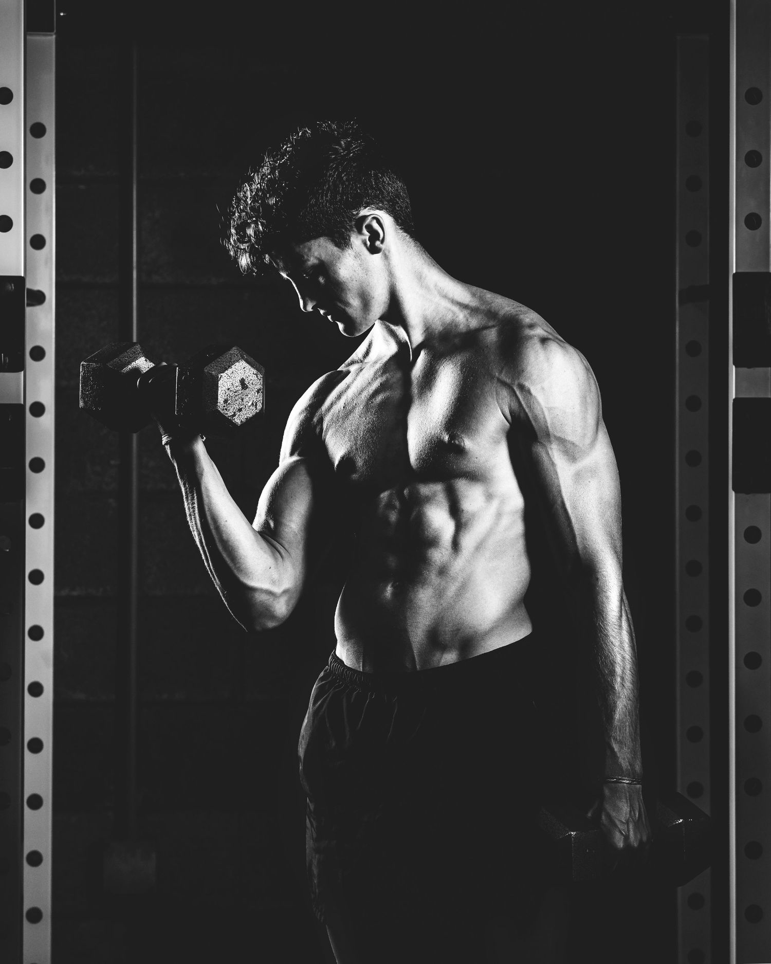 Athletic figure performing dumbbell curls in dark gym with dramatic lighting. Middle TN senior photographer