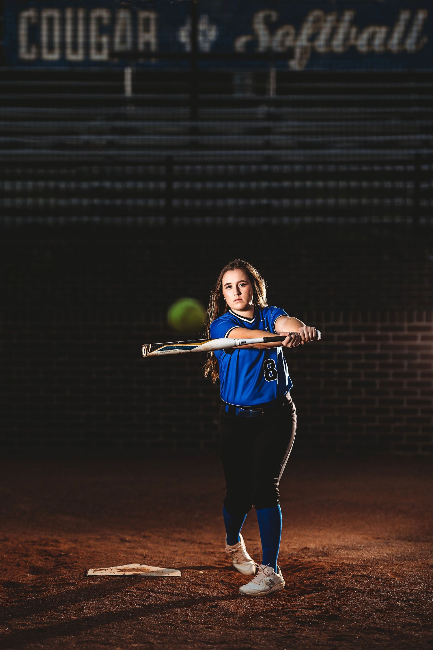 Softball player in blue uniform poses on dirt field at night. Middle TN senior photographer