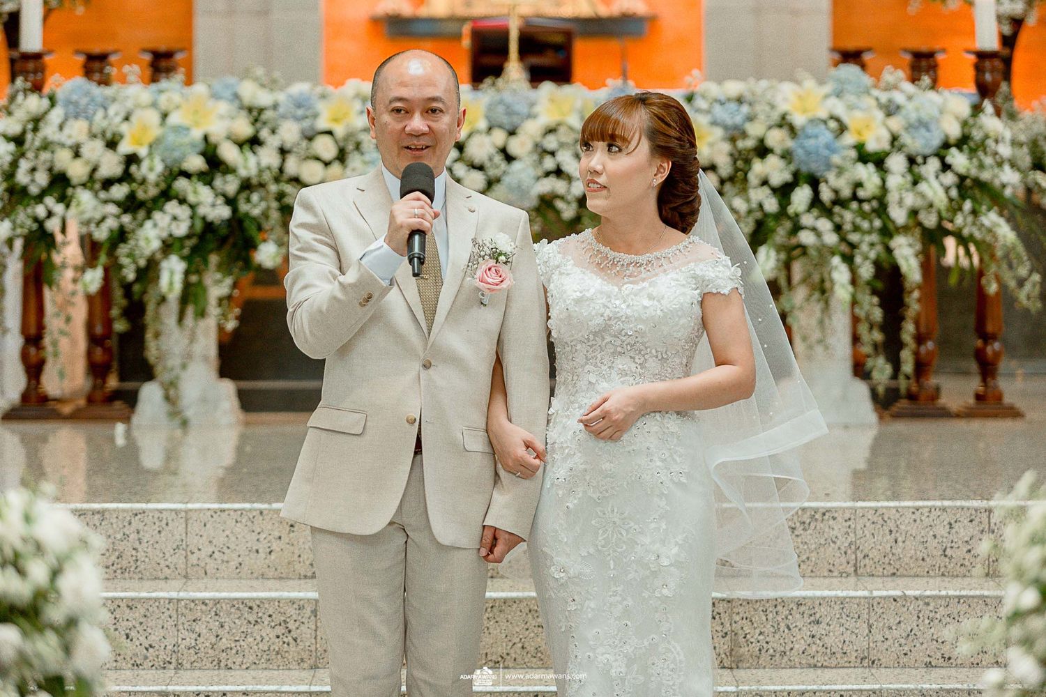 A couple shares a moment on stage during their wedding reception with floral decor.