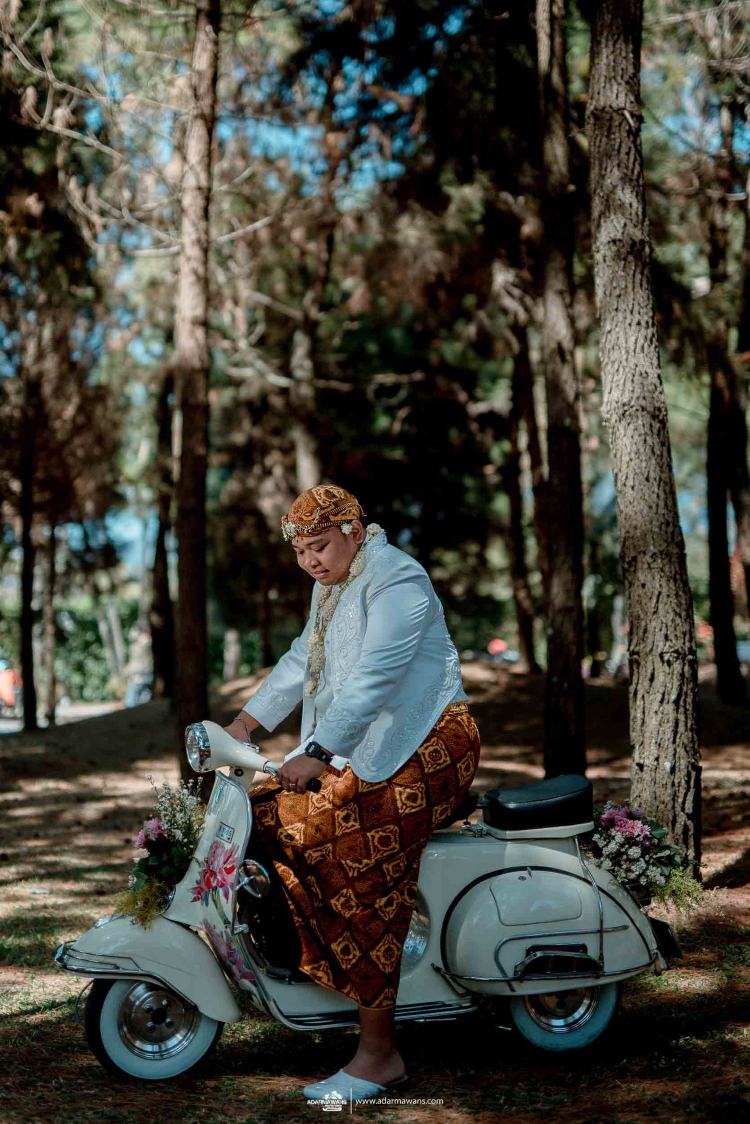 Person in light blue jacket rides vintage Vespa scooter through pine forest.