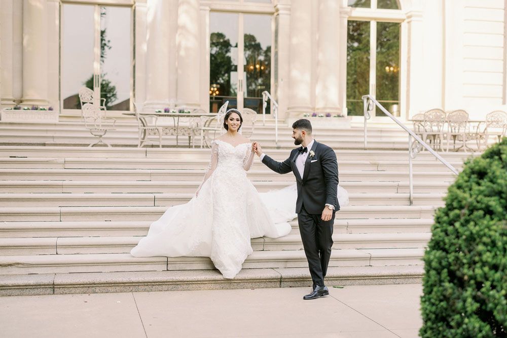 Couple descending grand white stone steps in formal wedding attire.