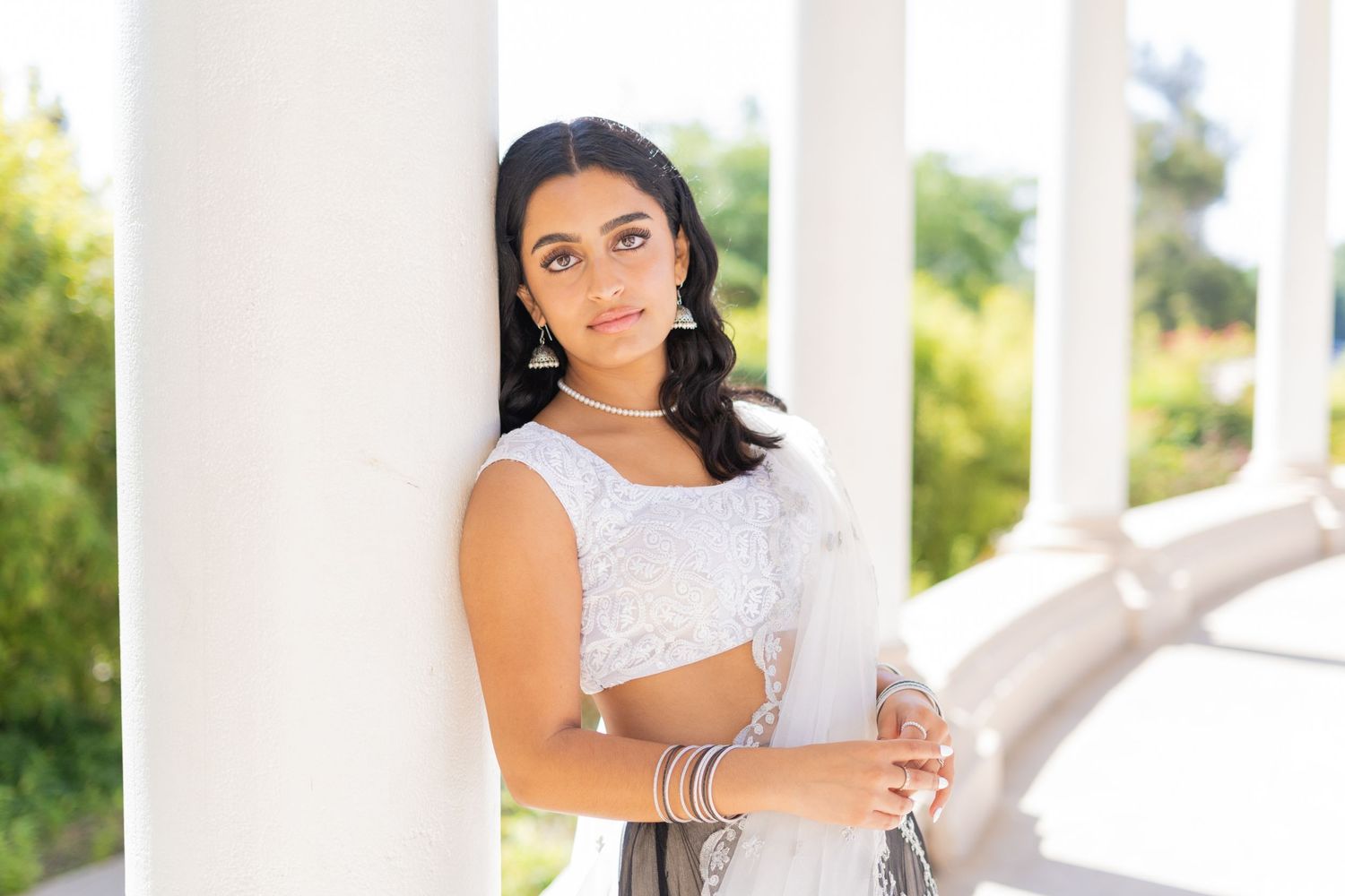 A high school senior in white crop top and dark skirt posing against white pillars outdoors.