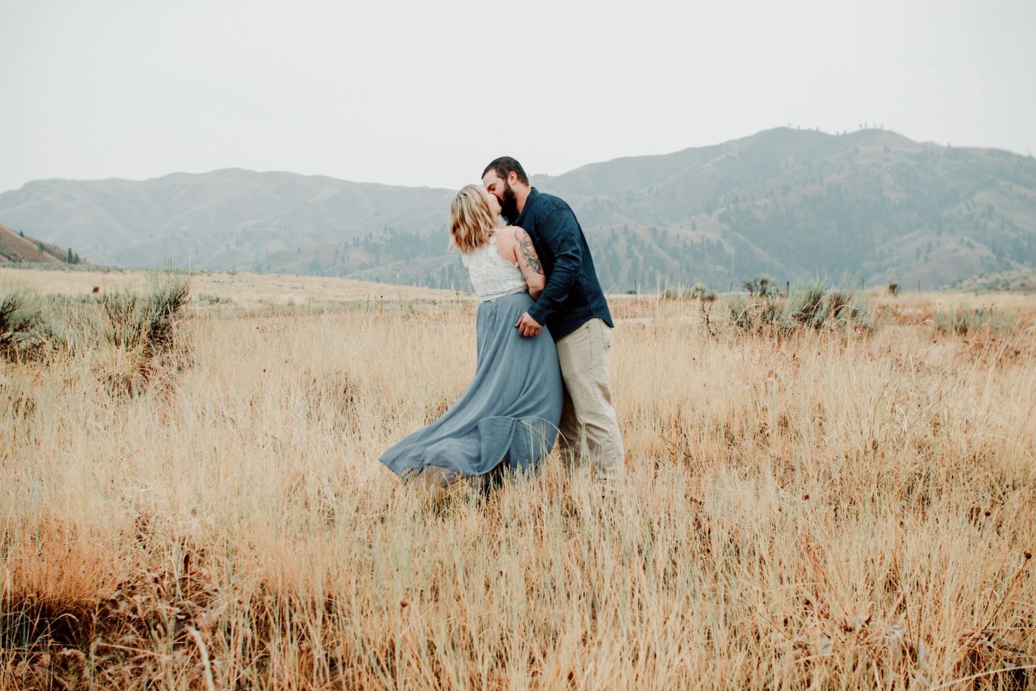 Silhouettes of a couple embracing in a golden field with mountains in the background.