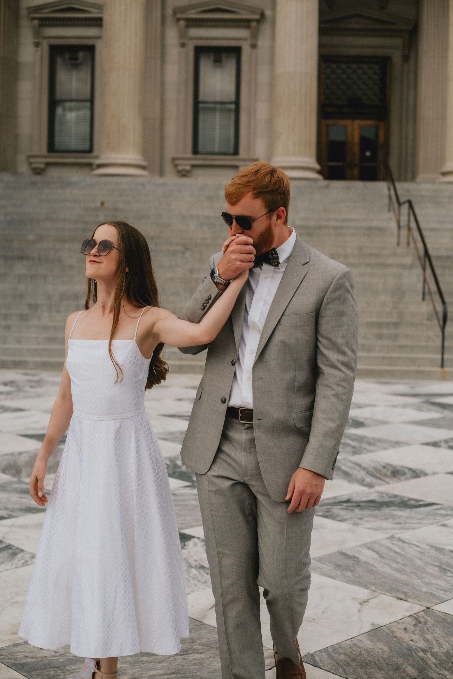 A couple wearing sunglasses walks across the Custom House in Charleston