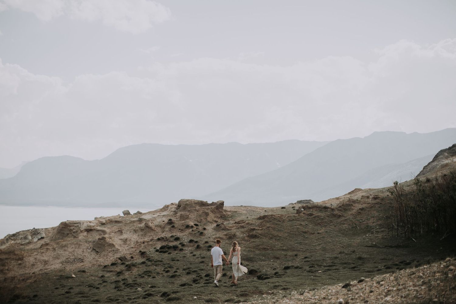 Distant figures on a rocky hillside with mountains and lake in the misty background.