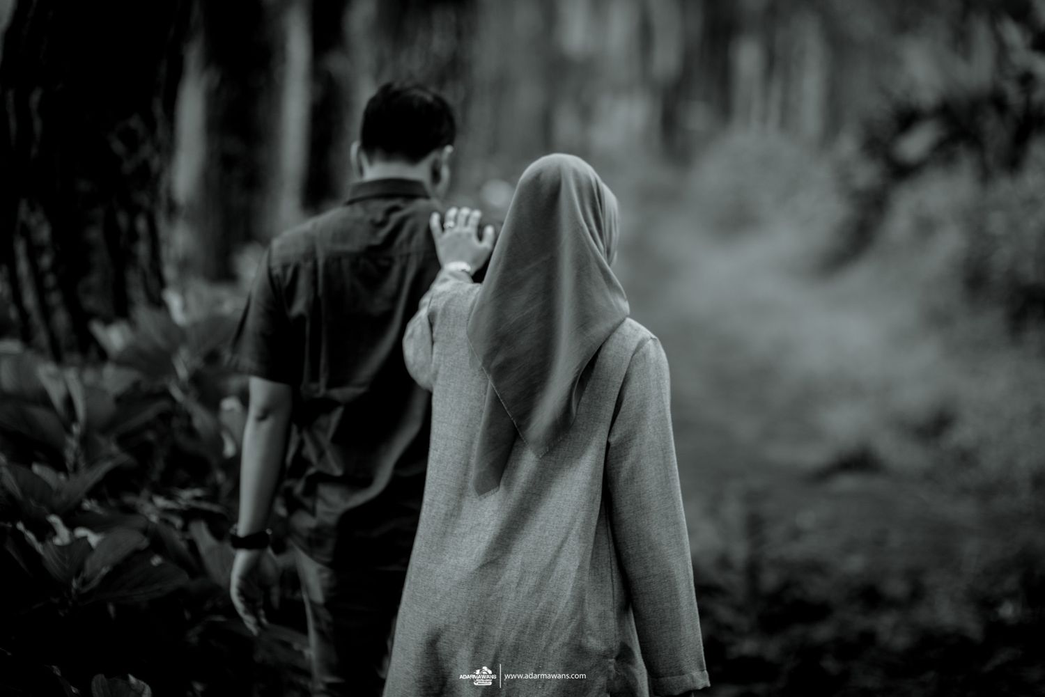 Two figures walking through a misty forest path in black and white.