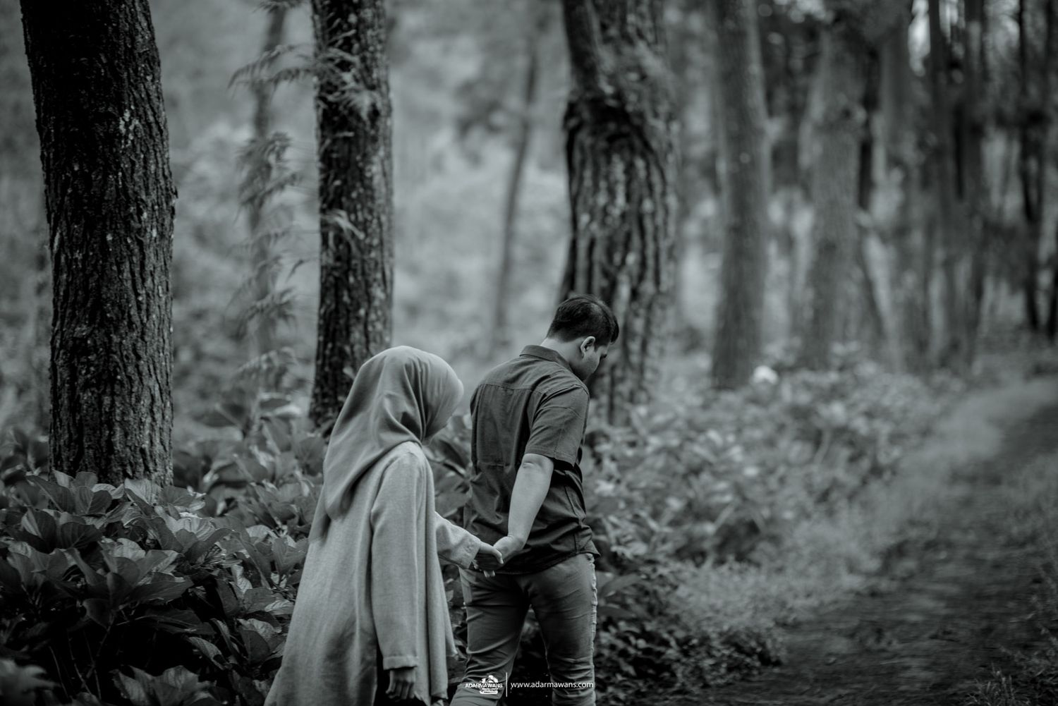 Two people walking hand in hand through a monochrome forest scene.